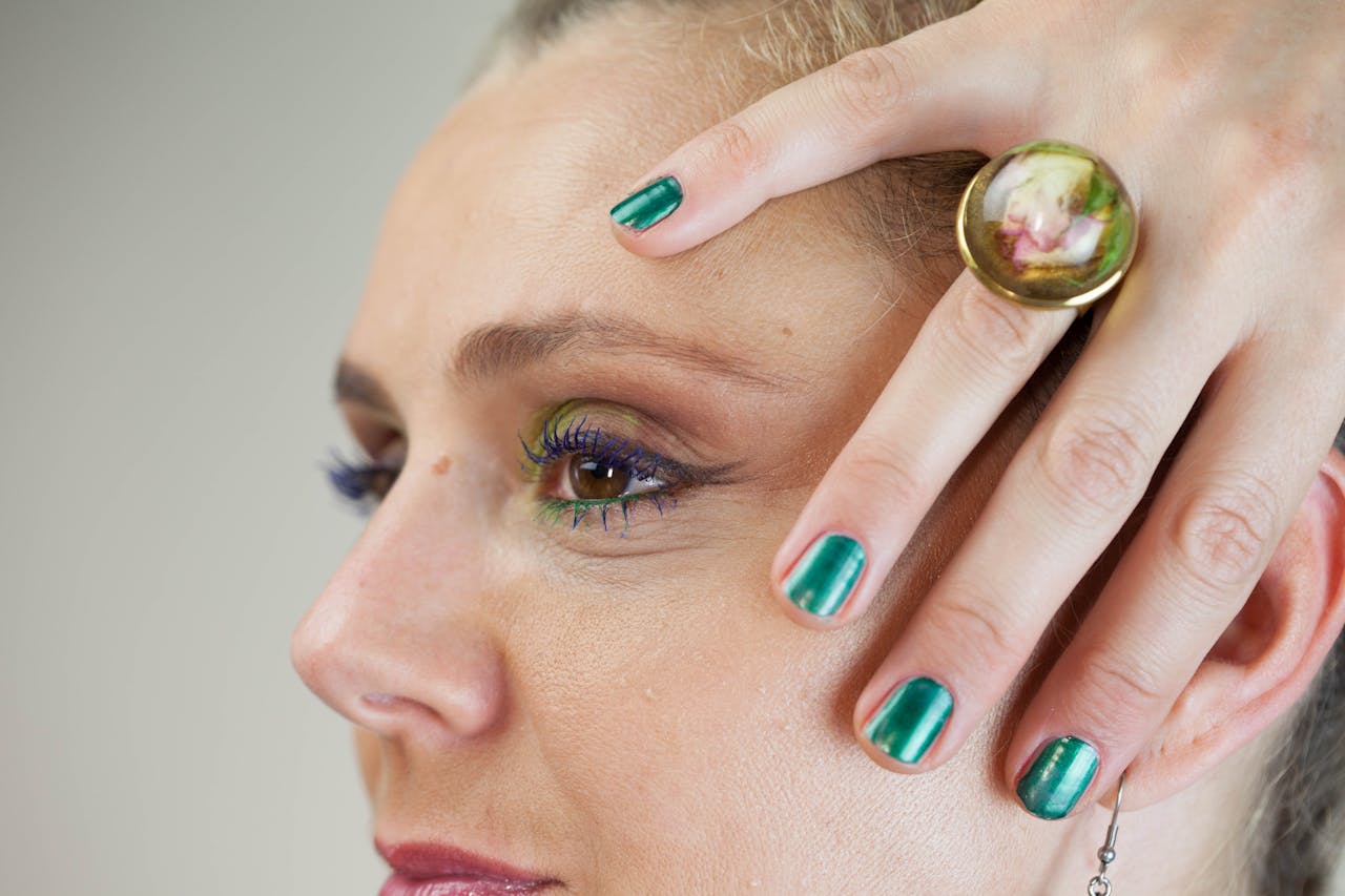 Stylish close-up portrait showcasing bold makeup, green nail polish, and a unique ring accentuating beauty and fashion.
